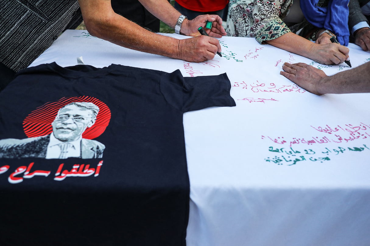 Le 23 mai 2025, à Tunis, en Tunisie, des militants inscrivent des messages d’espoir et de soutien à Ahmed Souab sur une nappe blanche lors d’un parloir symbolique organisé par sa famille. Cet événement rassemble des dizaines de militants, d’artistes, de membres de la société civile, de journalistes et de représentants d’organisations de défense des droits humains venus témoigner de leur solidarité. Ahmed Souab, connu pour son opposition au président tunisien Kaïs Saïed, est détenu pour terrorisme après avoir publiquement dénoncé la sévérité des peines prononcées dans l’affaire dite de « complot contre la sûreté de l’État ». Il fait partie de l’équipe juridique qui défend plusieurs personnalités politiques de premier plan, condamnées en première instance à de lourdes peines de prison dans cette même affaire.