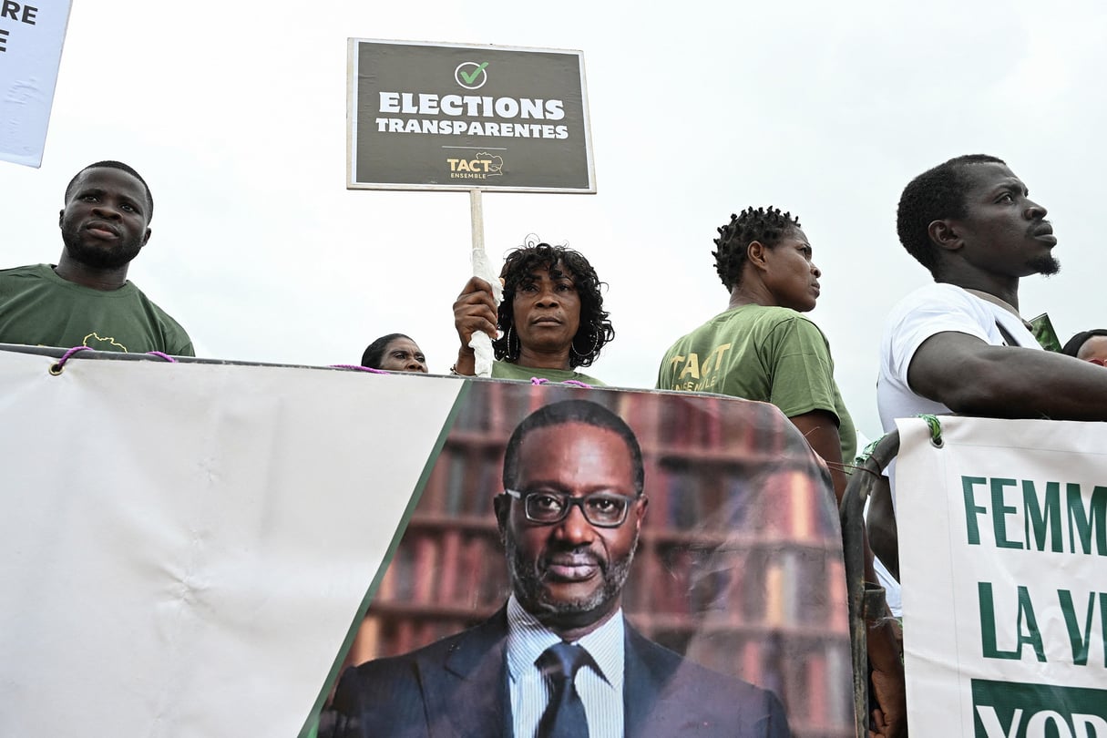 Un partisan de la Coalition pour l’alternance pacifique-Côte d’Ivoire tient une pancarte à côté d’une bannière politique représentant le président du Parti démocratique de Côte d’Ivoire (PDCI), Tidjane Thiam, lors de leur première réunion à Abidjan, le 31 mai 2025. © Sia KAMBOU/AFP