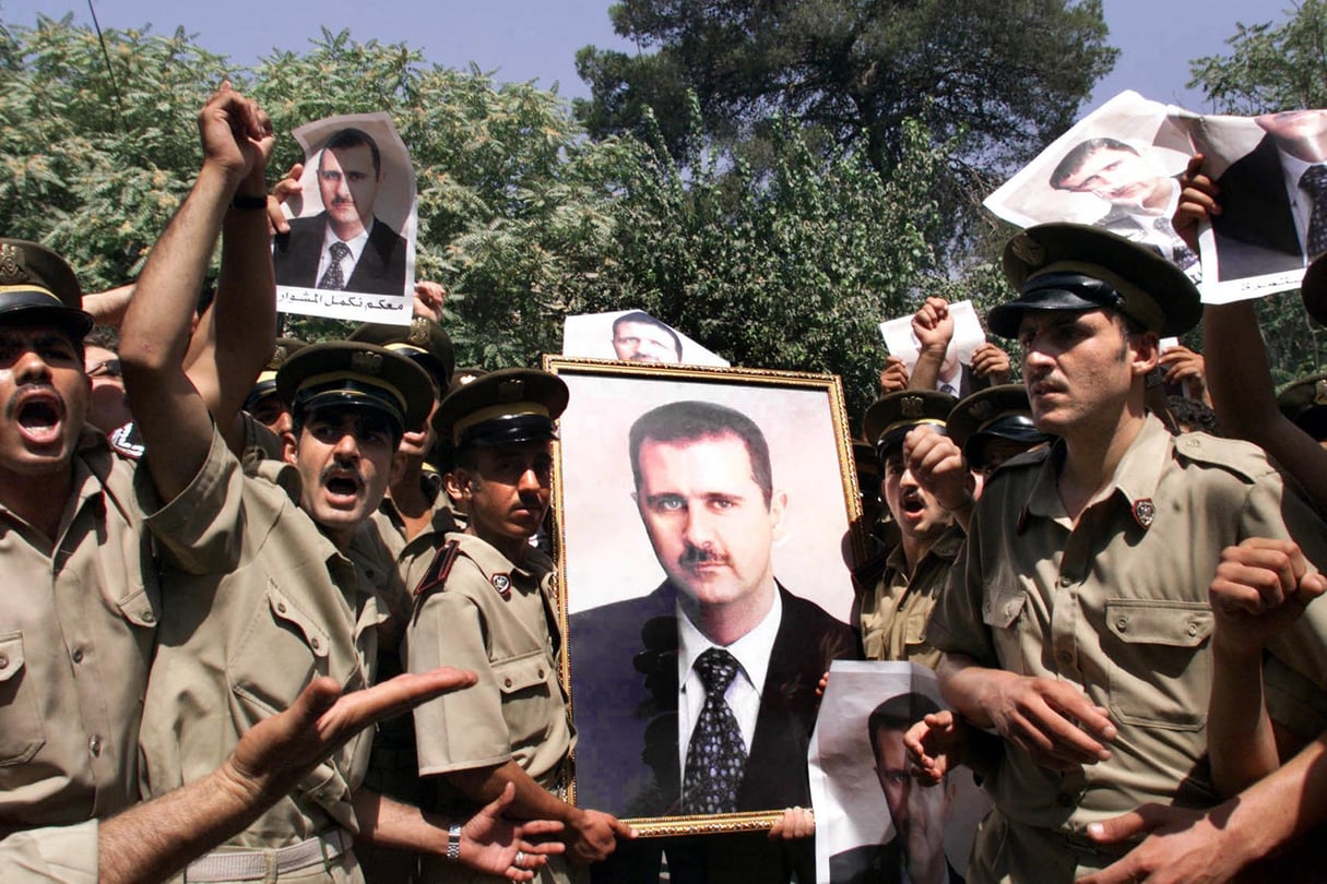 Policiers syriens brandissant des affiches à l’effigie de Bachar al-Assad devant un bureau de vote, à Damas, le 10 juillet 2000, à l’occasion d’un référendum qui donnera le pouvoir au fils du défunt Hafez al-Assad. © Joseph Barrack/AFP