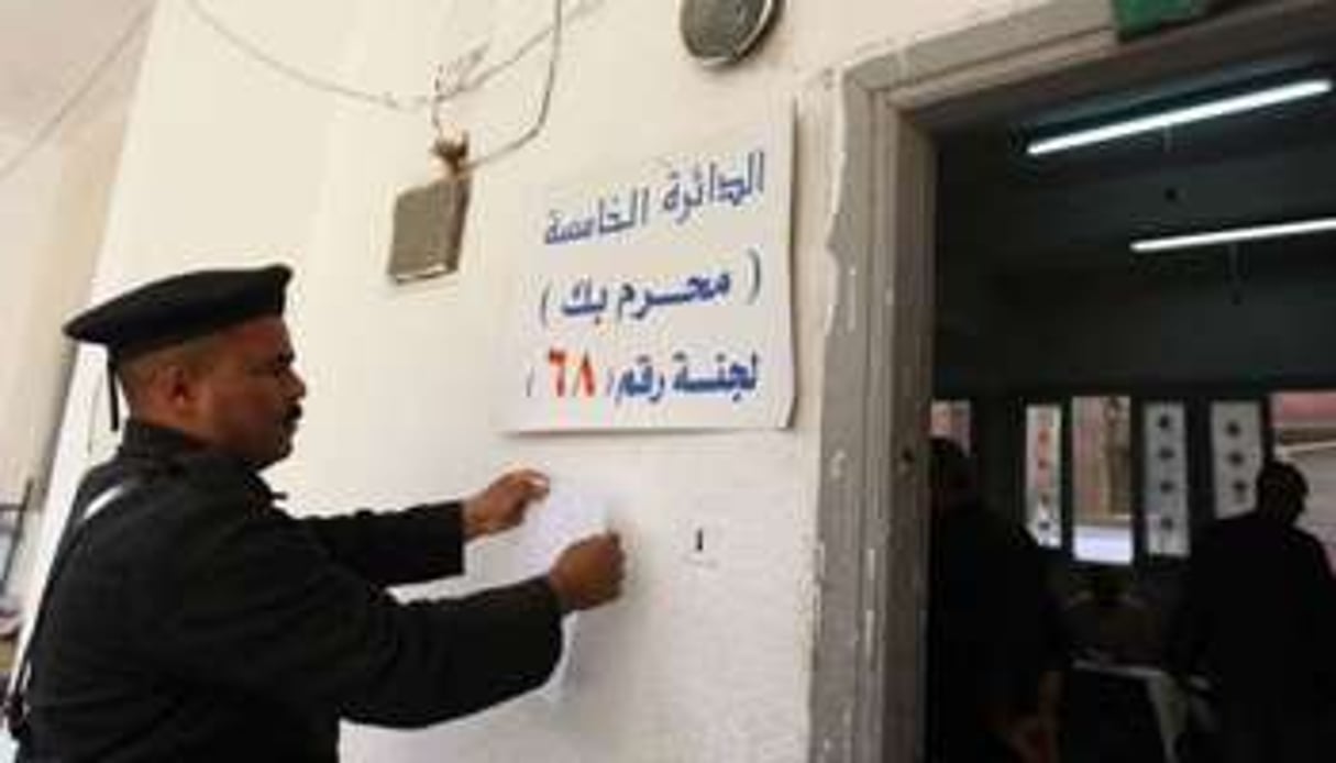 Un policier égyptien pose une affiche devant un bureau de vote à Alexandrie, le 28 novembre. © AFP