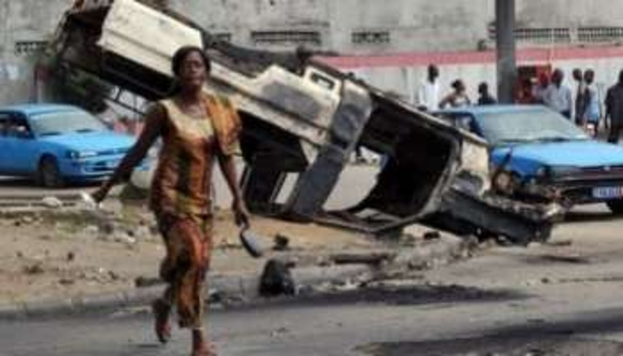 Jeune-femme devant une voiture de l’ONU brûlée, le 30 décembre à Abidjan. © AFP