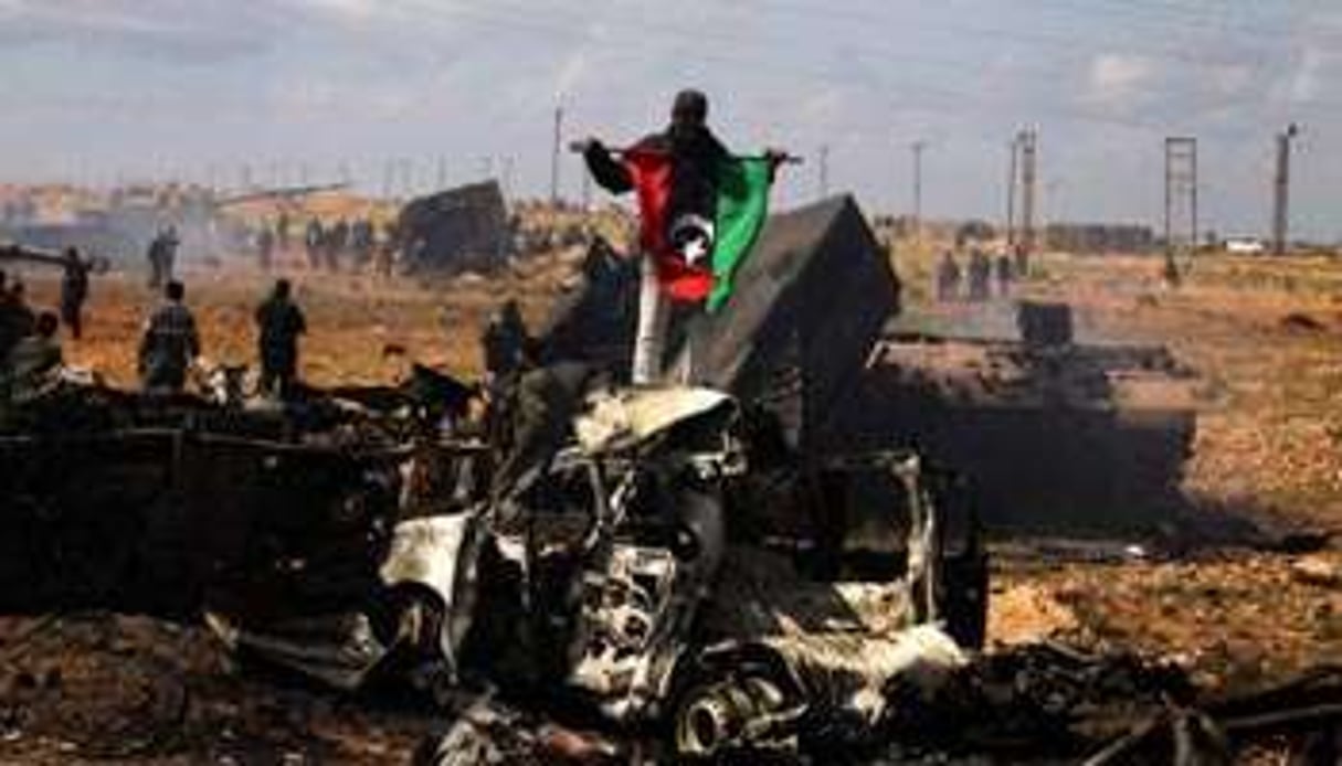 Des insurgés libyens au milieu des carcasses de chars de l’armée de Kaddafi, le 20 mars. © AFP