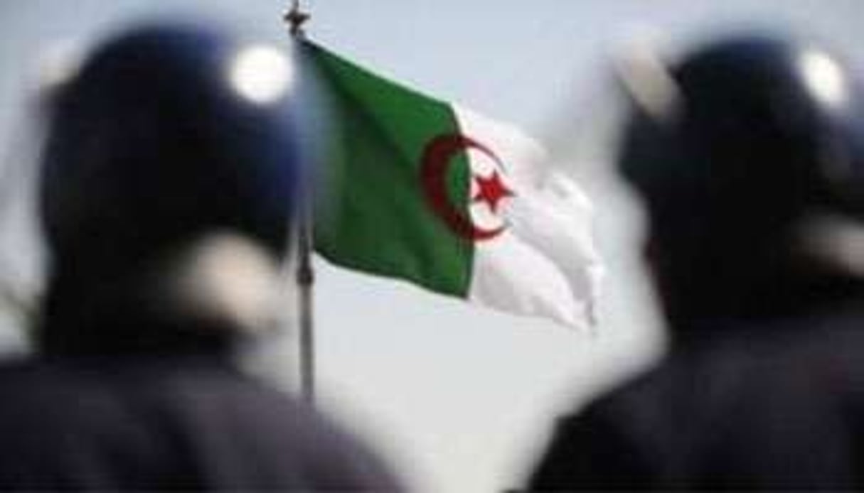 Deux policiers devant le drapeau algérien. © Farouk Batiche/AFP