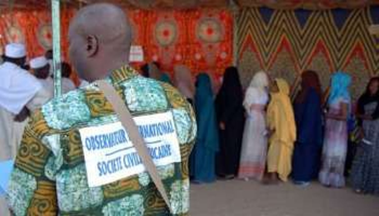 Un observateur international regarde des électeurs en train de faire la queue à un bureau de vote. © AFP