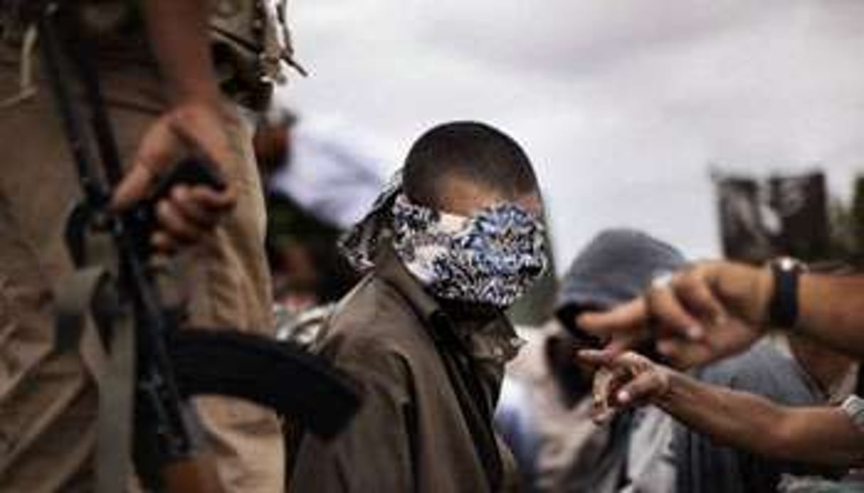 Un combattant pro-Kadhafi, les yeux bandés, est gardé par un membre de la rébellion libyenne. © AFP