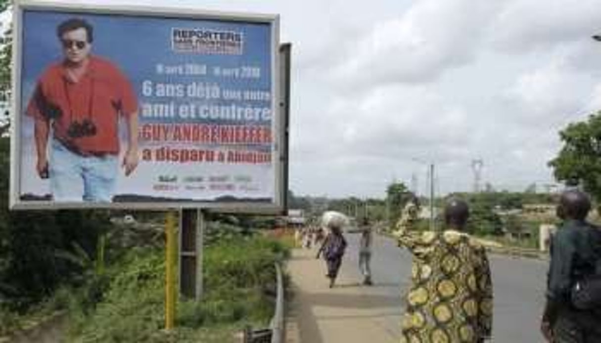 Des Ivoiriens regardent une affiche montrant Guy Andre Kieffer disparu à Abidjan en 2004. © AFP