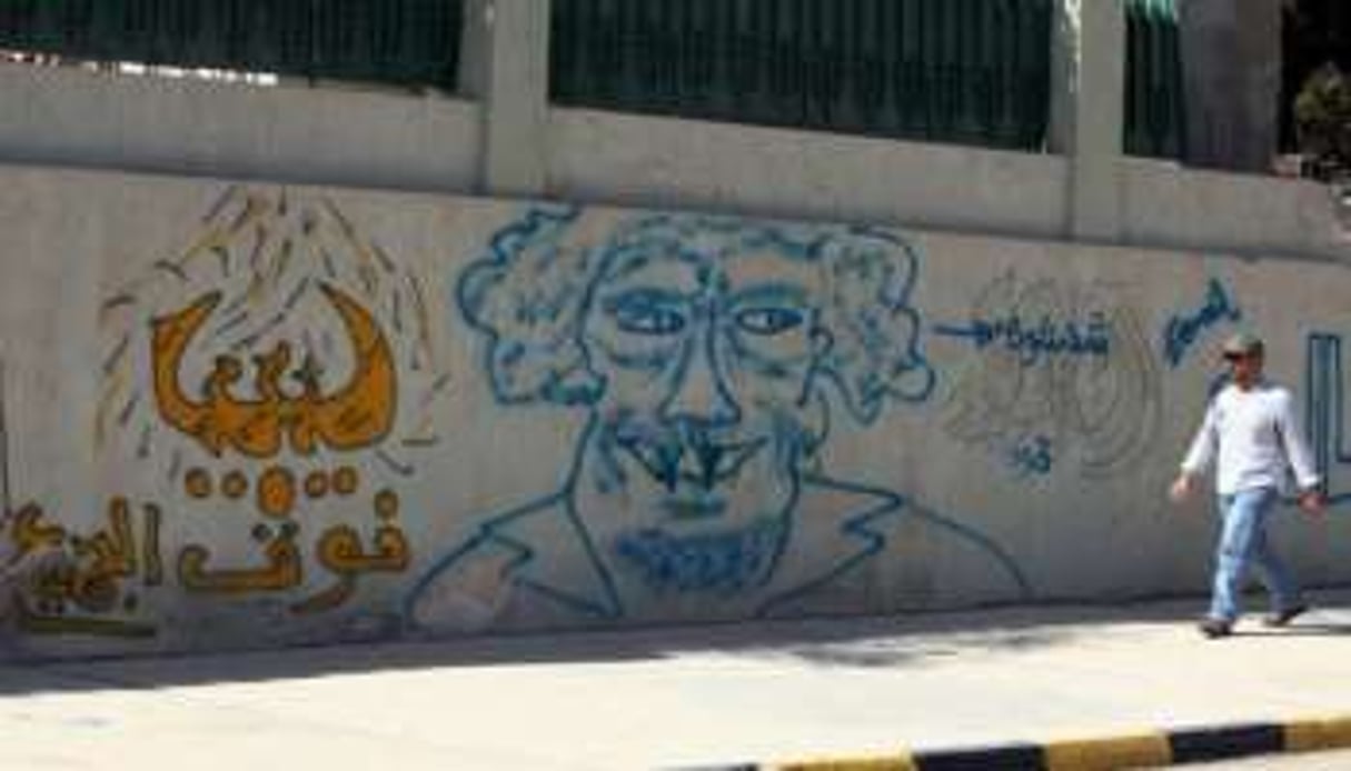 Un Libyen passe devant un graffiti représentant Mouammar Kaddafi. © AFP