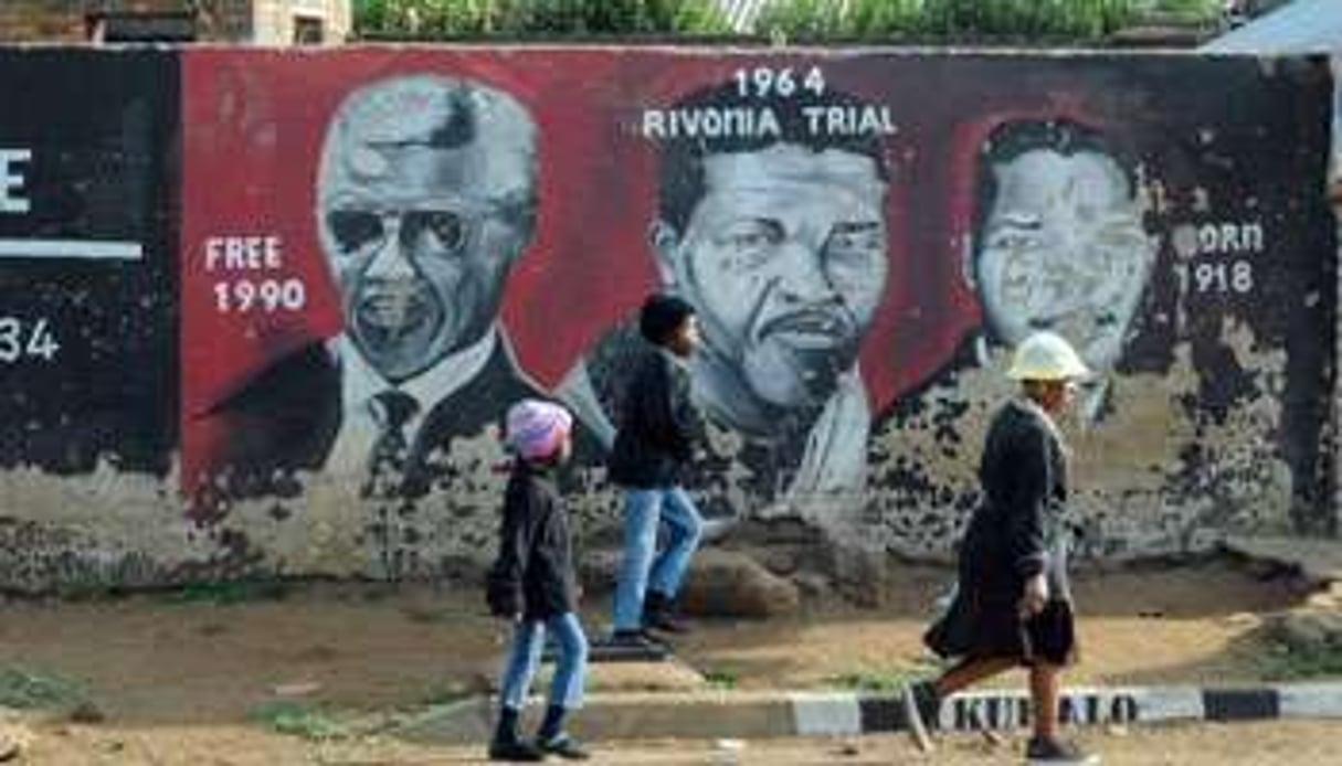 Des Sud-Africains passent devant un mur où a été peint le portrait de Mandela. © AFP