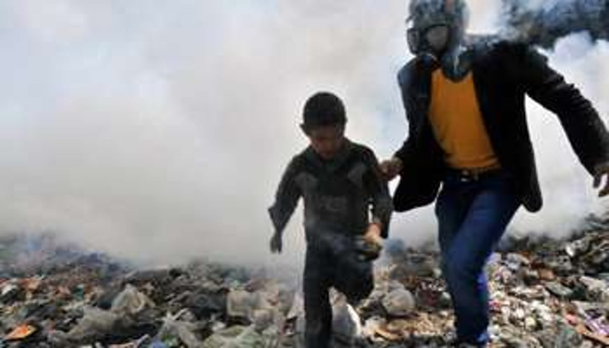 Un homme équipé d’un masque à gaz et un jeune garçon courent dans une rue d’Alep. © AFP