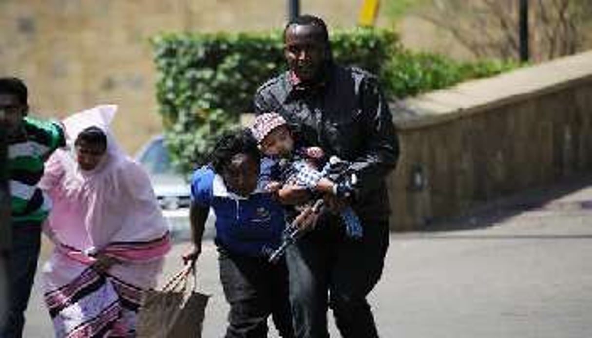 Un policier escorte des personnes qui quittent un centre commercial de Nairobi. © AFP