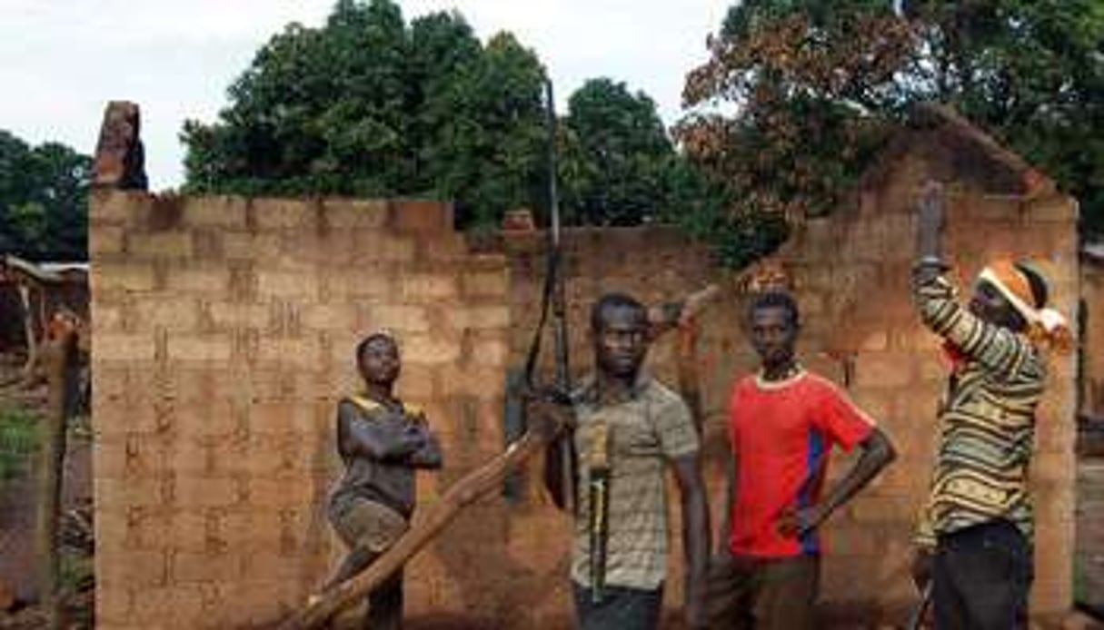 De jeunes hommes armés patrouillent près d’une maison incendiée à Bogangolo, le 11 octobre 2013. © Pacome Pabandji/AFP