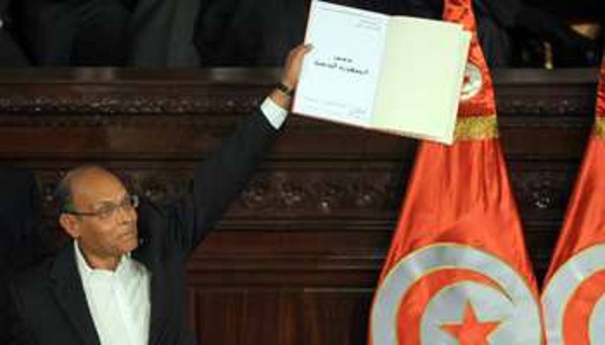 Le président tunisien Moncef Marzouki brandit un exemplaire signé de la nouvelle Constitution. © AFP