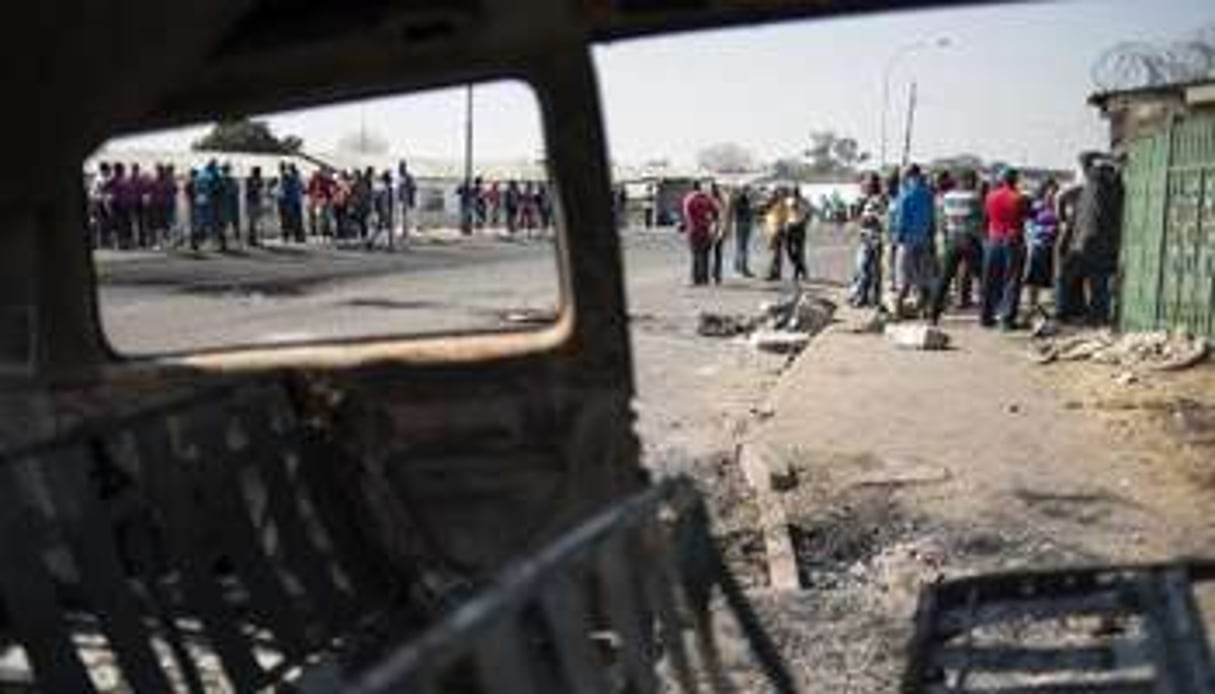 Des grévistes du secteur de la métallurgie vus à travers la carcasse d’une voiture brûlée. © AFP