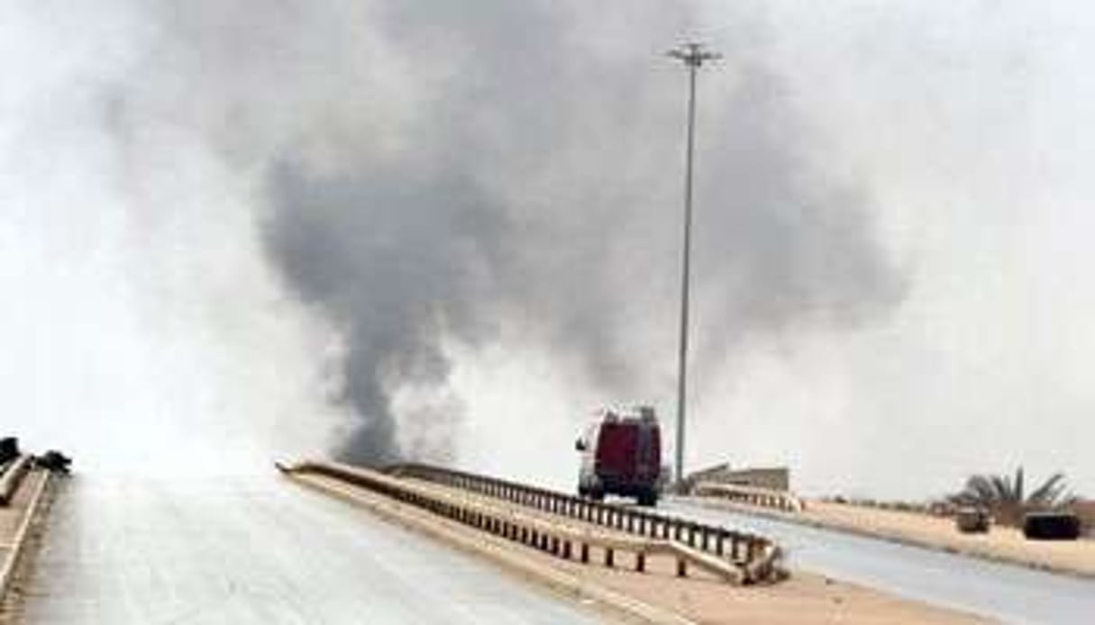 Un véhicule roule sur une route déserte alors que de la fumée s’élève de la ville de Benghazi. © AFP