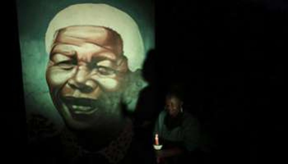 Une habitante de Soweto éclaire à la bougie une peinture murale de Nelson Mandela, le 4 décembre. © Siphiwe Sibeko/Reuters