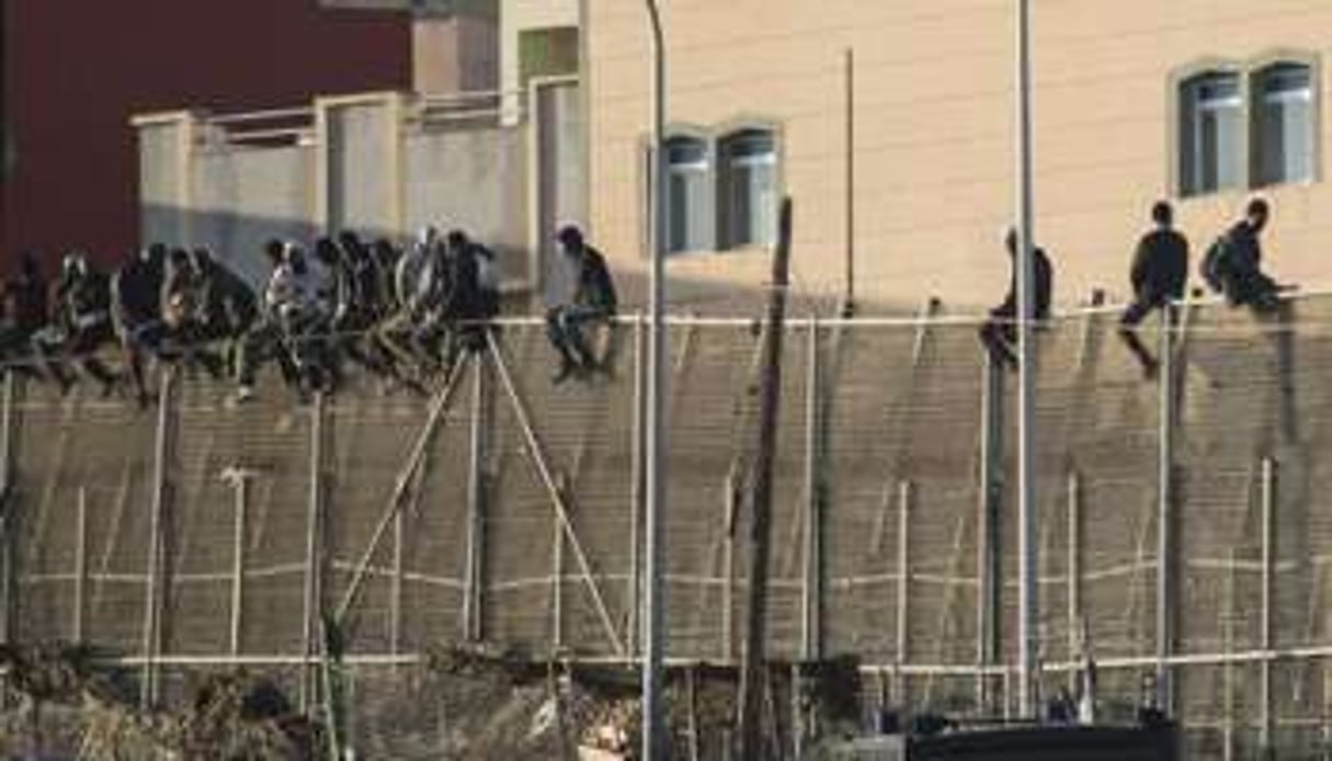 Des migrants assis sur la barrière interdisant l’accès à Melilla. © AFP