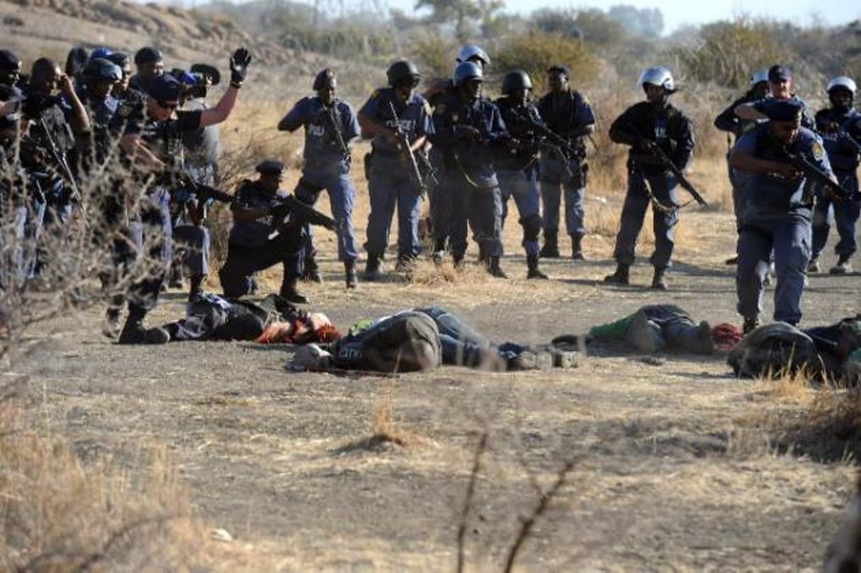 Des policiers sud-africains se tiennent près des corps de mineurs tombés à Marikana. © AFP