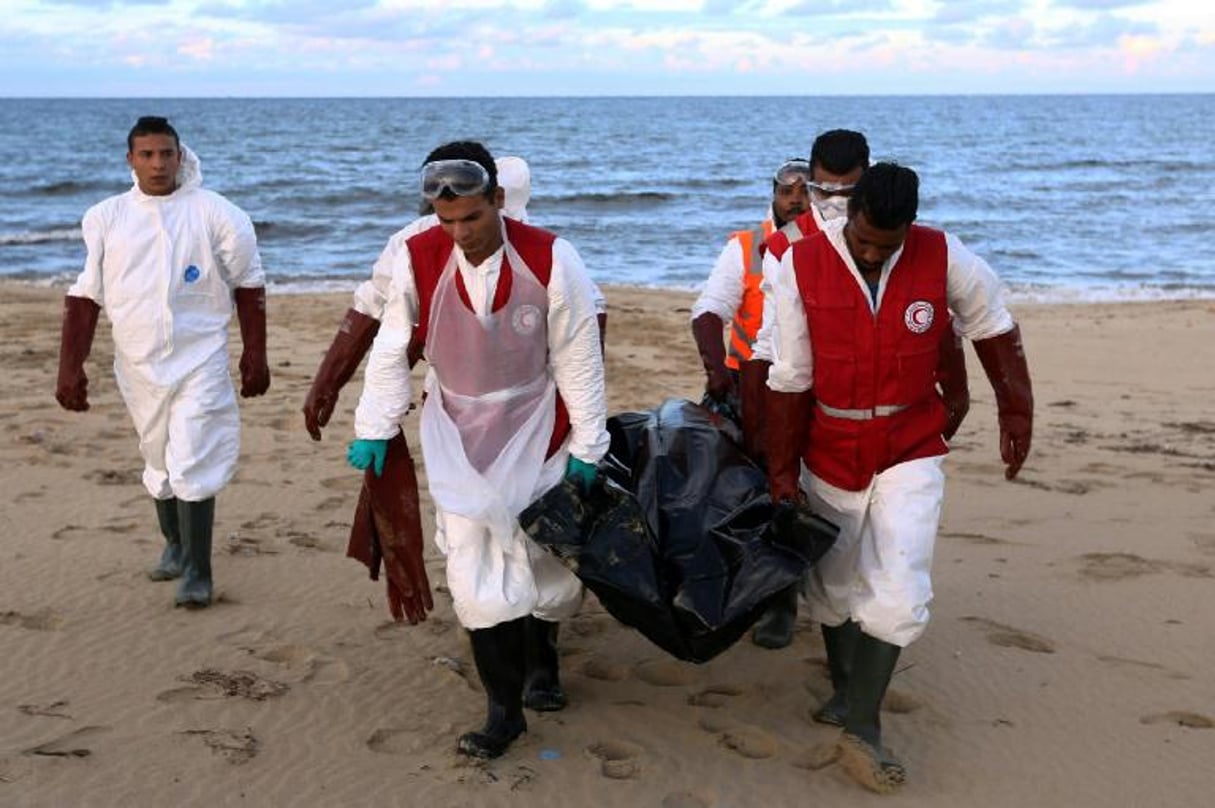 Des membres du Croissant-Rouge libyen transportent le corps d’un migrant mort par noyade, le 11 décembre 2016 sur une plage, à l’est de Tripoli. © Stringer/AFP