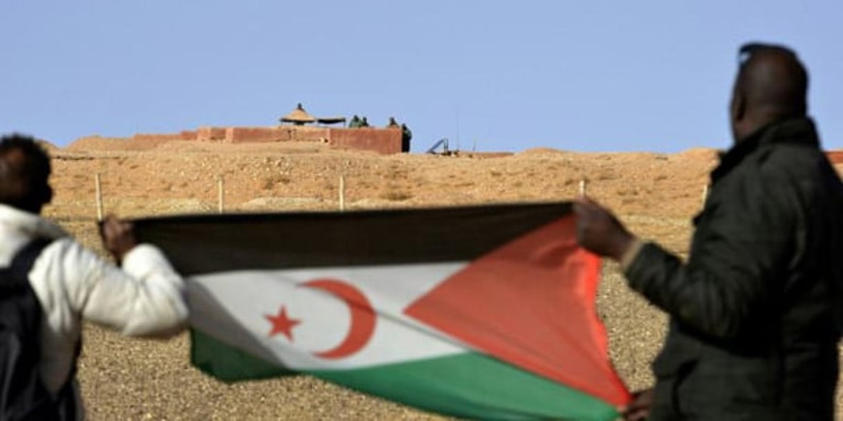 Des Saharaouis tiennent le drapeau du Front Polisario en face de soldats marocains qui montent la garde le long du « mur des sables » qui sépare le Marcoc du Sahara occidental, le 3 février 2017 à Al-Mahbes. © Ryad Kramdi / AFP