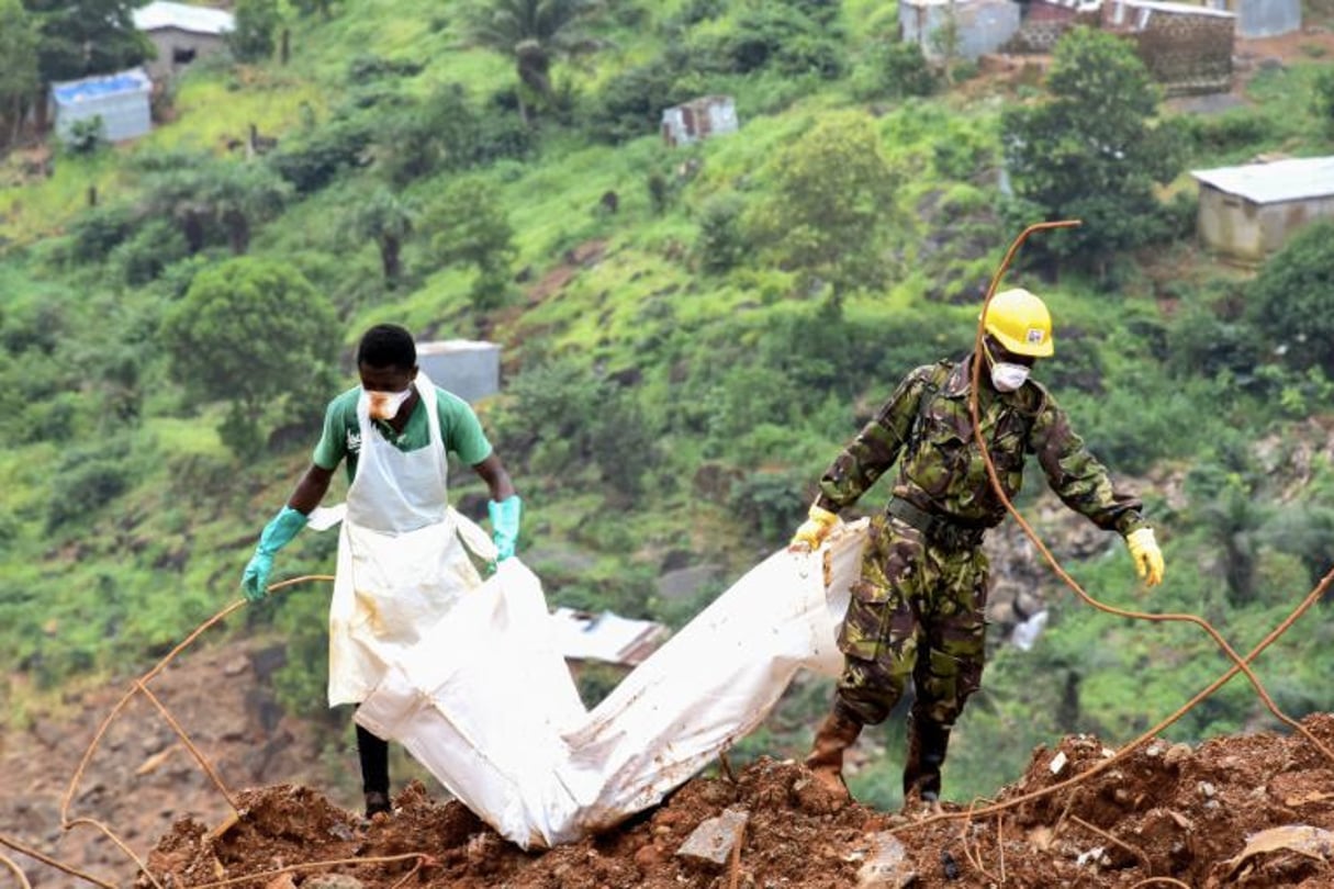 Un bénévole et un soldat portent le 19 août 2017 le corps d’une victime des inondations qui ont frappé Freetown, en Sierra Leone, quelques jours plus tôt. © AFP / SEYLLOU