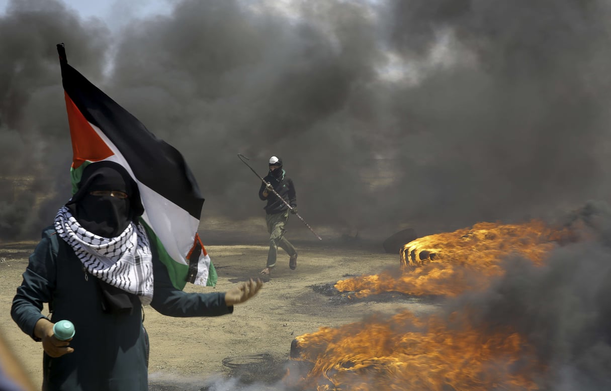Une femme brandit un drapeau palestinien alors qu'un manifestant brûle des pneus près de la frontière israélienne, à l'est de Khan Younis, dans la bande de Gaza, lundi 14 mai 2018, avant l'inauguration de l'ambassade des Etats-Unis à Jérusalem. &copy; Adel Hana/AP/SIPA
