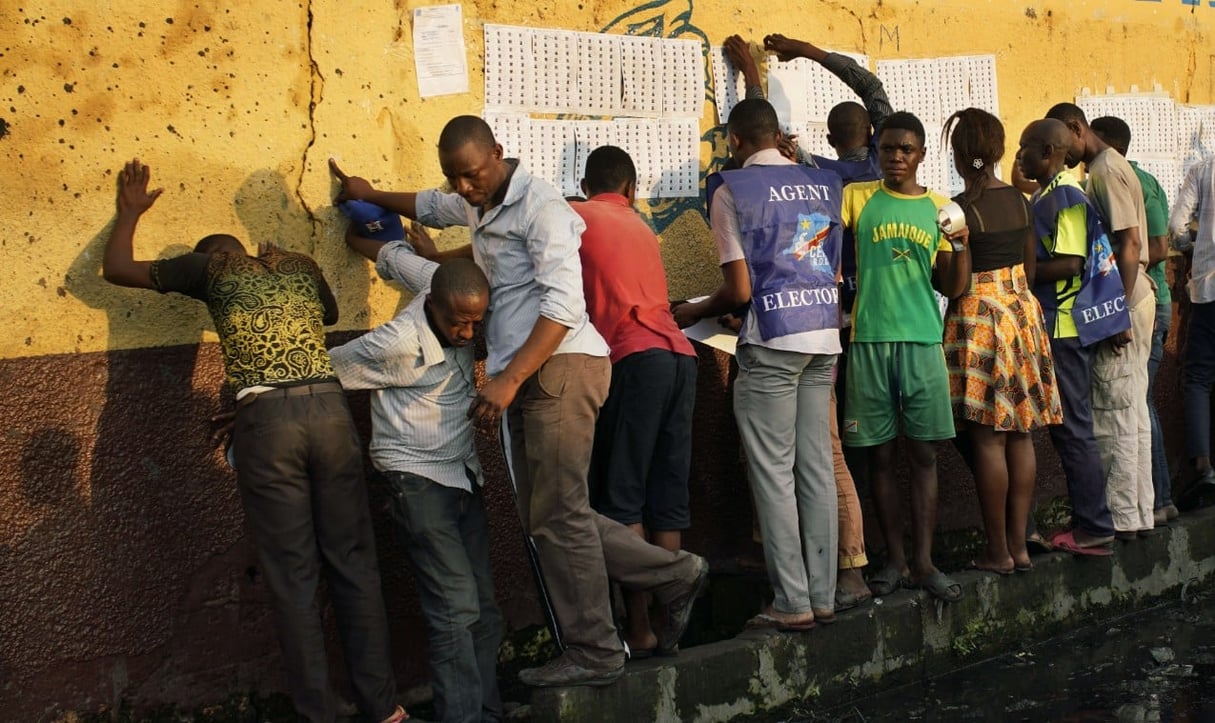 Les fonctionnaires électoraux enregistrent la liste des inscriptions des électeurs sur le mur de l’école primaire Les Anges à Kinshasa, au Congo, alors que les électeurs commencent à vérifier leur nom, le dimanche 30 décembre 2018. © Jerome Delay/AP/SIPA