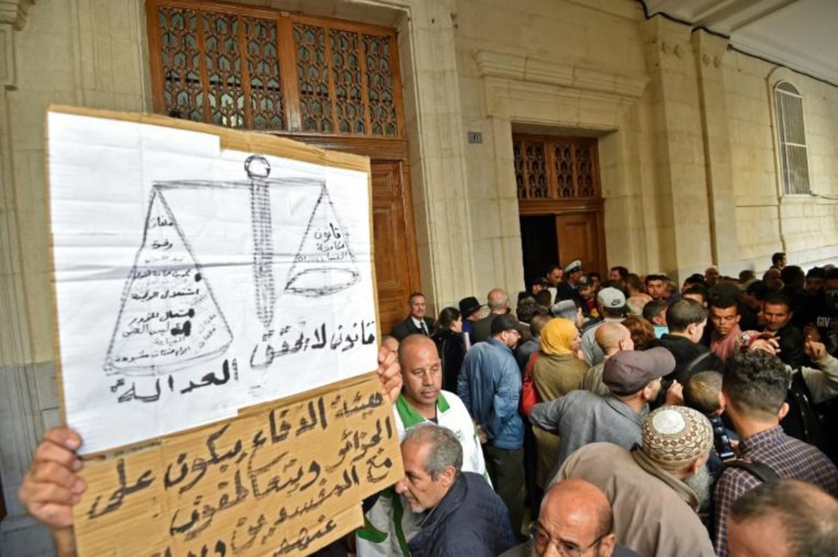 Des Algériens brandissent une pancarte réclamant justice, devant l’entrée du tribunal de Sidi M’hamed, le 2 décembre 2019 à Alger. © RYAD KRAMDI/AFP