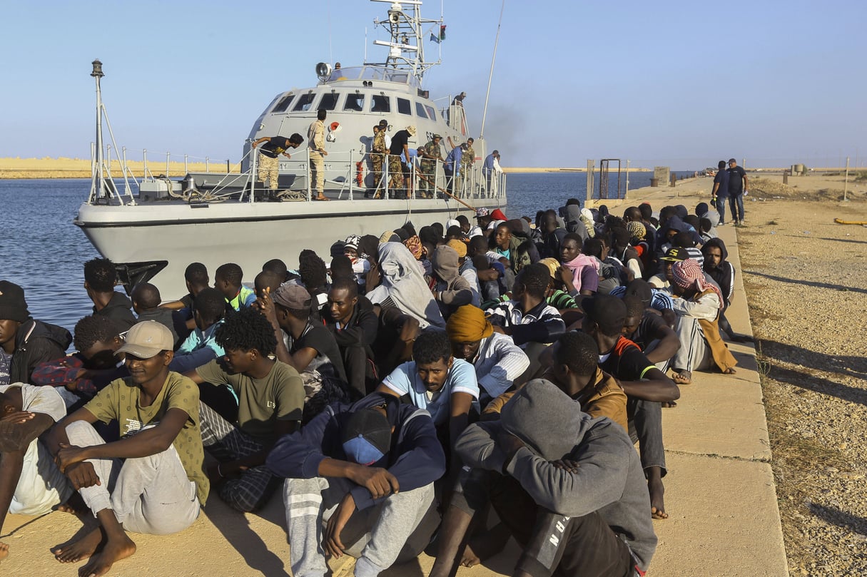 Des migrants secourus sont assis à côté d’un bateau des garde-côtes dans la ville de Khoms, en Libye, en octobre 2019. © Hazem Ahmed/AP/SIPA