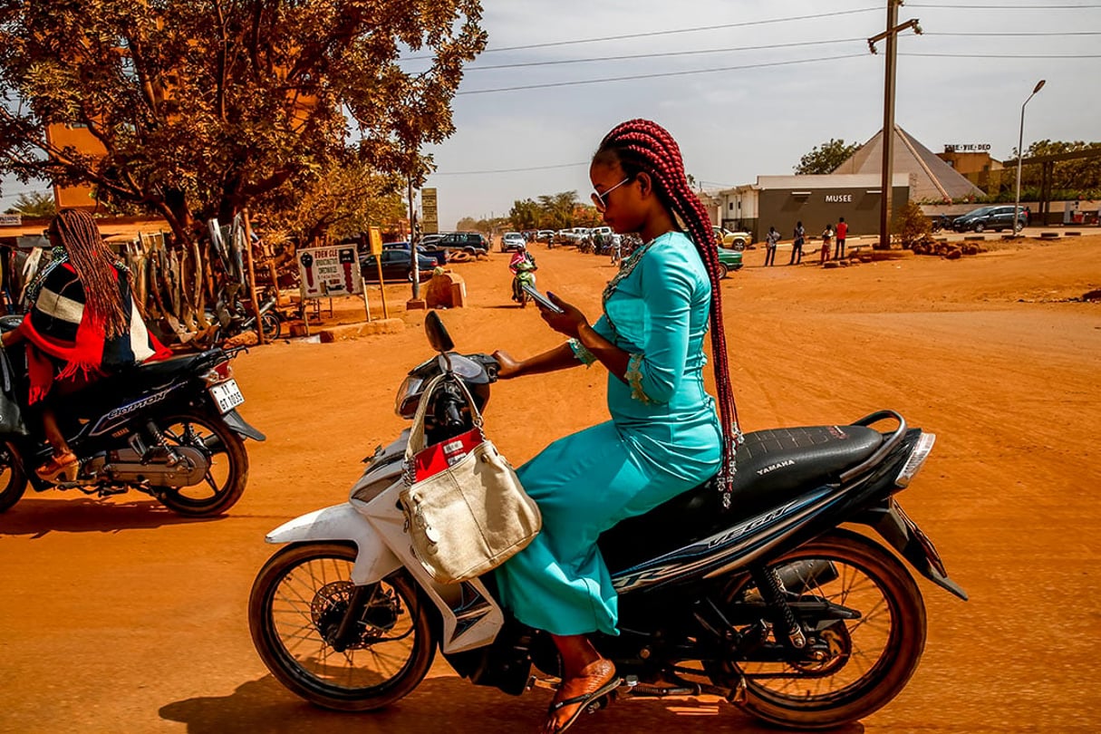 L’Afrique subaharienne compte 548 millions d’utilisateurs du mobile money en 2020. Ici, jeune femme sur son scooter consultant son téléphone portable à Ouagadougou, Burkina Faso. © Getty Images