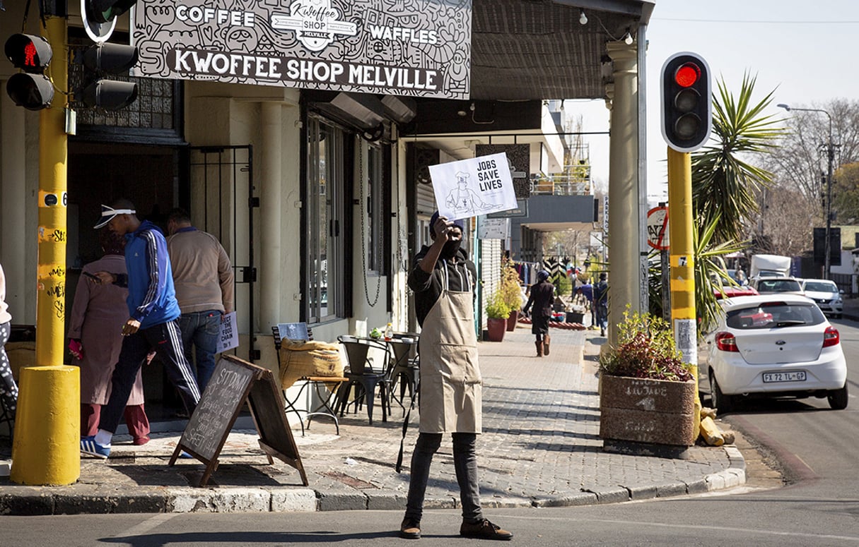 Un homme tient un panneau sur lequel est écrit « Les emplois sauvent des vies » à l’extérieur d’un restaurant à Johannesburg, en Afrique du Sud, le 22 juillet 2020. © Yeshiel/Xinhua/REA