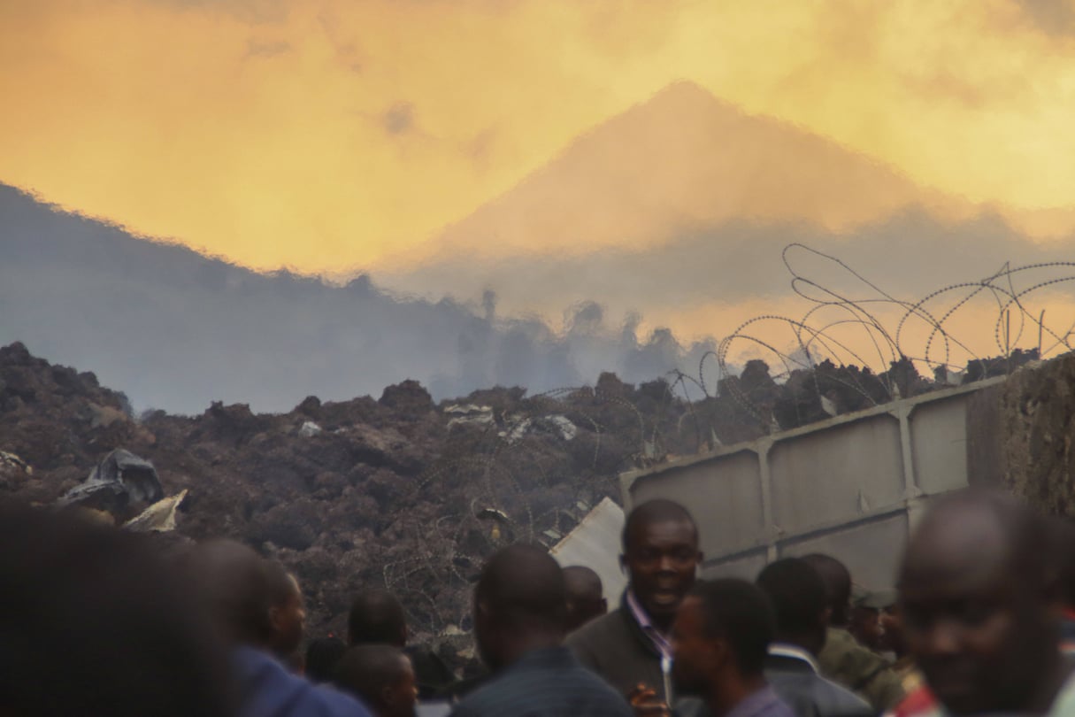 Les résidents vérifient les dégâts causés par la lave de l’éruption nocturne du volcan Nyiragongo, en arrière-plan, à Buhene, dans la banlieue de Goma, en RDC, aux premières heures du dimanche 23 mai 2021. © Justin Kabumba/AP/SIPA