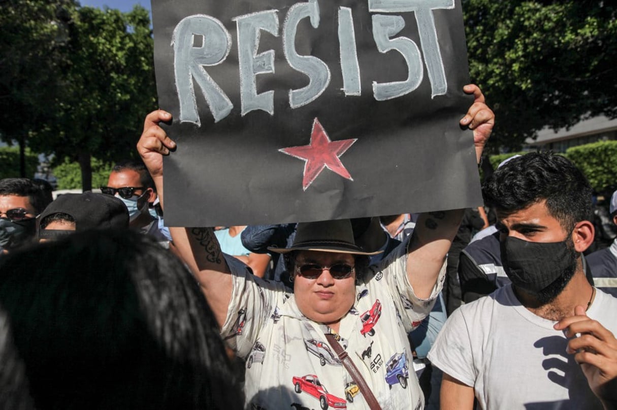 La militante LGBTQI+, queer et féministe Rania Amdouni brandit une pancarte qui dit ‘resist’ devant les membres des forces de sécurité lors d’une manifestation qui s’est tenue avenue Habib Bourguiba à Tunis, le 12 juin 2021, pour protester contre les brutalités policières, après une vidéo de la police déshabille et bat un mineur. © Chedly Ben Ibrahim/AFP