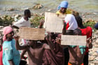 Des migrants africains, bloqués sur le bord de mer à la frontière entre la Libye et la Tunisie à Ras Jedir, brandissent des pancartes demandant l’aide, le 26 juillet 2023. © Mahmud TURKIA / AFP