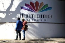Un couple se tient sous le logo de MultiChoice affiché à l'extérieur du siège social de l'entreprise à Randburg, en Afrique du Sud, le 9 juin 2025.