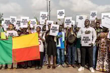 Des jeunes brandissent des pancartes et des drapeaux et chantent l'hymne national lors d'un rassemblement organisé par la jeunesse sur la place Amazone à Cotonou, le 13 décembre 2025, en soutien au président béninois Patrice Talon et à la préservation de la démocratie. Des centaines de personnes, principalement des jeunes, se sont rassemblées samedi dans la capitale béninoise, Cotonou, pour dénoncer la tentative de coup d'État de dimanche dernier. Agitant des drapeaux nationaux et le poing levé, les participants scandaient des slogans tels que « Plus jamais ça » et réclamaient la paix, la stabilité et le respect de l'ordre constitutionnel. (Photo : Yanick Folly / AFP)