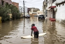 Un jeune garçon utilise une vieille planche de surf pour se frayer un chemin dans les rues inondées après les premières grandes pluies de la saison à Dakar, le 20 juillet 2022. © JOHN WESSELS/AFP