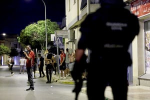 Un homme fume tandis que des gens se rassemblent dans une rue sous la surveillance d'un policier, dans un contexte de troubles anti-migrants suite à une agression contre un homme âgé par des assaillants inconnus plus tôt dans la semaine, à Torre Pacheco, en Espagne, le 13 juillet 2025.