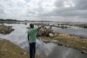 Un habitant montre des déchets en plastique sur des monticules de sable déversés dans la lagune par le ruissellement des eaux usées et des pluies sur les rives de la lagune Ébrié, dans le village de Beago, à Yopougon, Abidjan, le 20 juillet 2022. © SIA KAMBOU/AFP