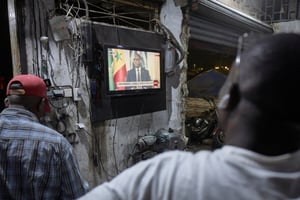 Des habitants de Dakar regardent l’ex-président sénégalais Macky Sall s’exprimer lors d’une conférence de presse retransmise à la télévision nationale, le 22 février 2024. © Michele Cattani / AFP