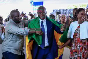 Brice Clotaire Oligui Nguema (au centre), drapé d’un drapeau gabonais, aux côtés de son épouse, Zita Nyangue Oligui Nguema (à droite), célèbre sa victoire à l’élection présidentielle, à Libreville, le 13 avril 2025. © Daniel BELOUMOU OLOMO / AFP