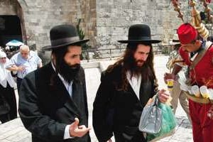 Deux juifs ultra-orthodoxes passant près d’un marchand arabe de jus caroube, à Jérusalem. © Menahem Kahana/AFP