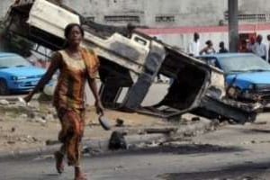 Jeune-femme devant une voiture de l’ONU brûlée, le 30 décembre à Abidjan. © AFP