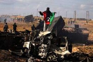 Des insurgés libyens au milieu des carcasses de chars de l’armée de Kaddafi, le 20 mars. © AFP