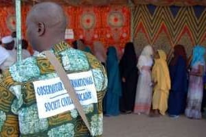 Un observateur international regarde des électeurs en train de faire la queue à un bureau de vote. © AFP