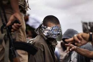 Un combattant pro-Kadhafi, les yeux bandés, est gardé par un membre de la rébellion libyenne. © AFP