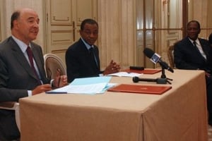 Pierre Moscovici et Charles Koffi Diby signent l’accord pour l’annulation de la dette ivoirienne en présence d’Alassane Ouattara à Paris. © Ana Aravelo/AFP