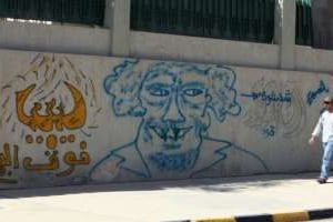 Un Libyen passe devant un graffiti représentant Mouammar Kaddafi. © AFP