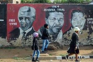 Des Sud-Africains passent devant un mur où a été peint le portrait de Mandela. © AFP