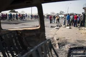 Des grévistes du secteur de la métallurgie vus à travers la carcasse d’une voiture brûlée. © AFP
