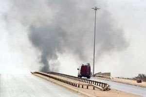 Un véhicule roule sur une route déserte alors que de la fumée s’élève de la ville de Benghazi. © AFP